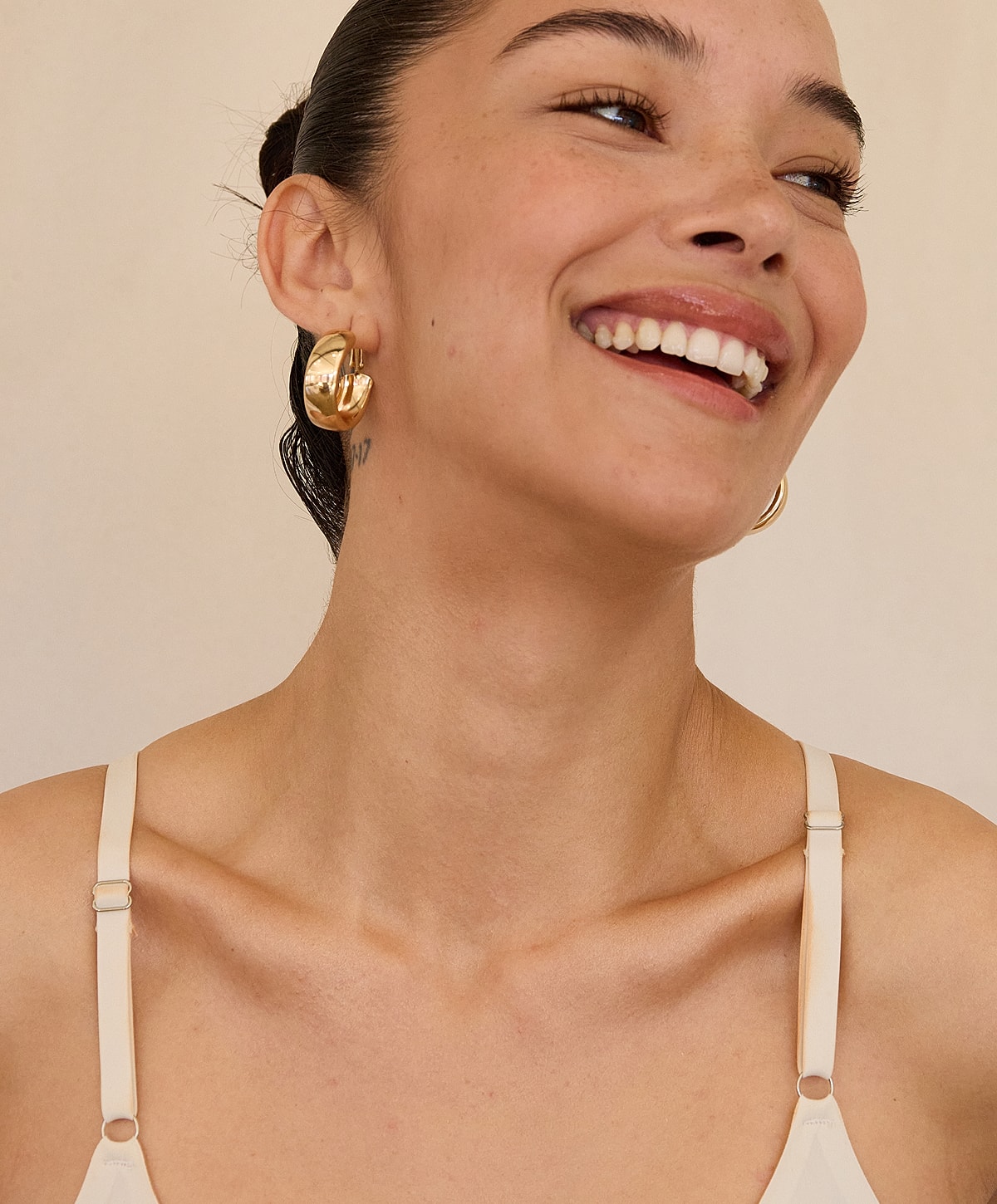 Smiling woman wearing gold earrings and tank top.