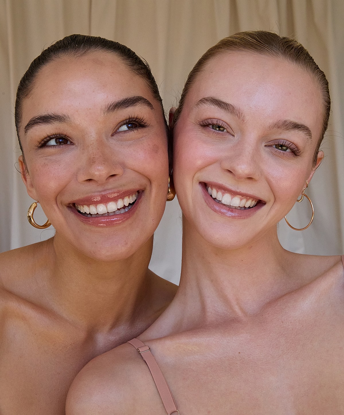 Two smiling women with glowing skin and earrings.