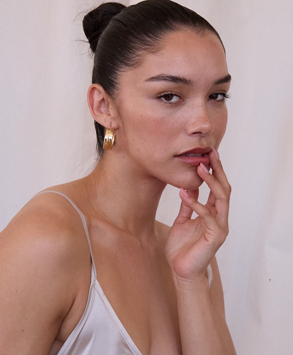 Model with hand on face, wearing hoop earrings.
