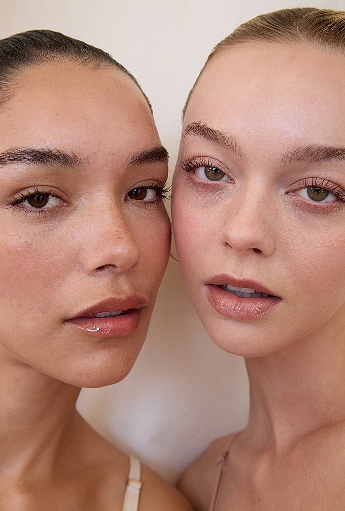 Two women posing closely together, natural makeup.