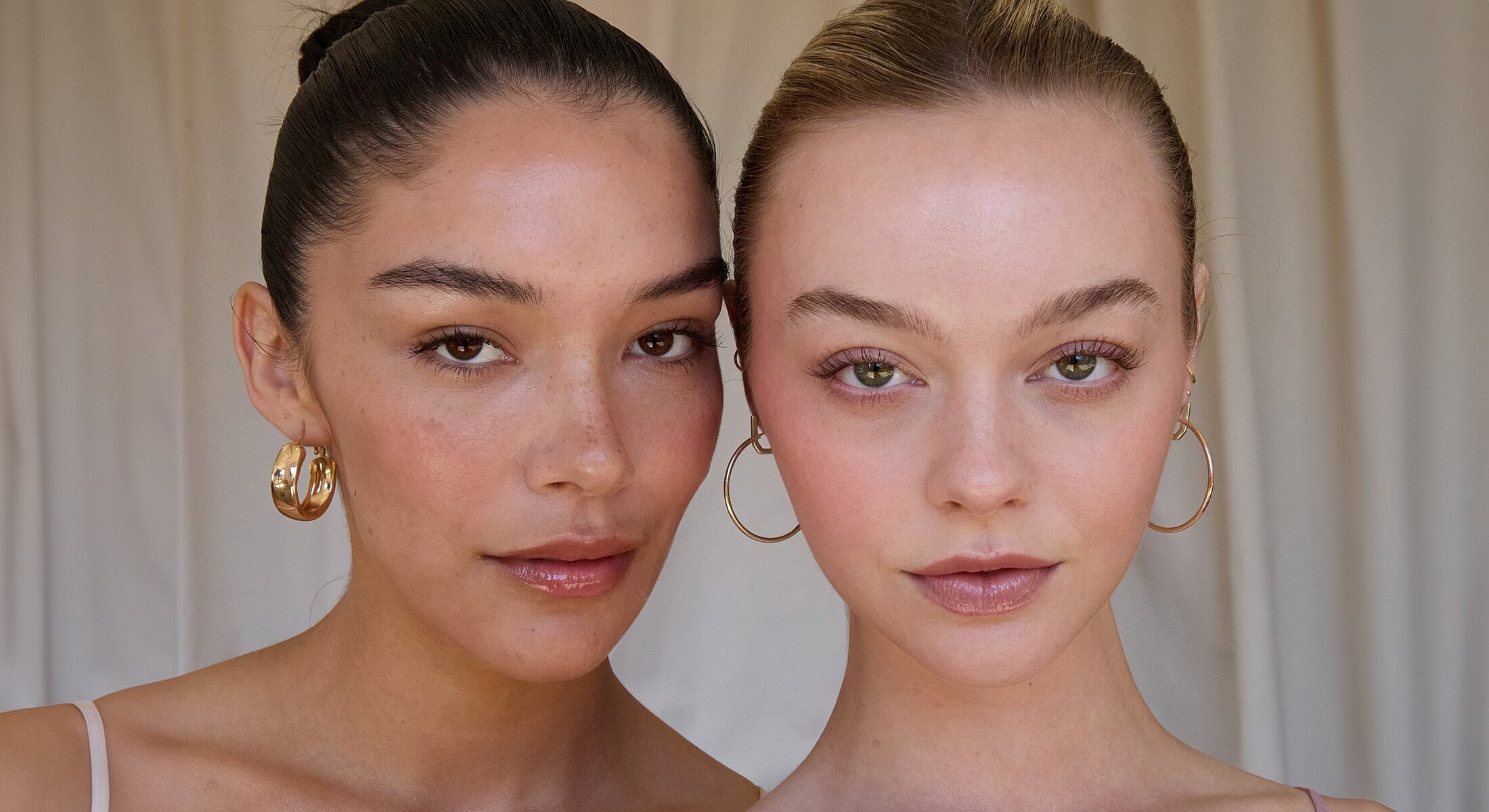 Two women with natural makeup and hoop earrings.