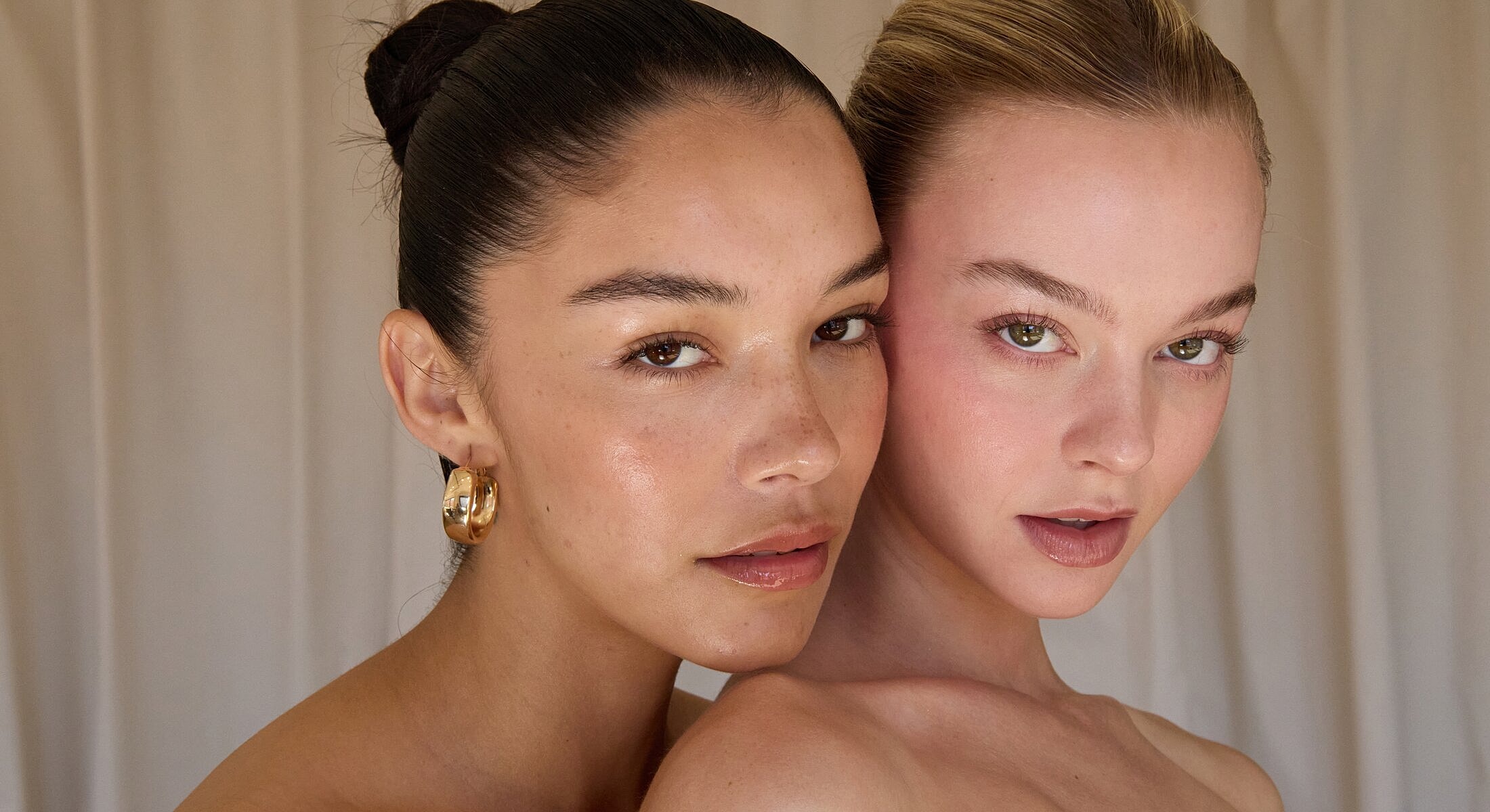 Two women posing closely, natural makeup look.