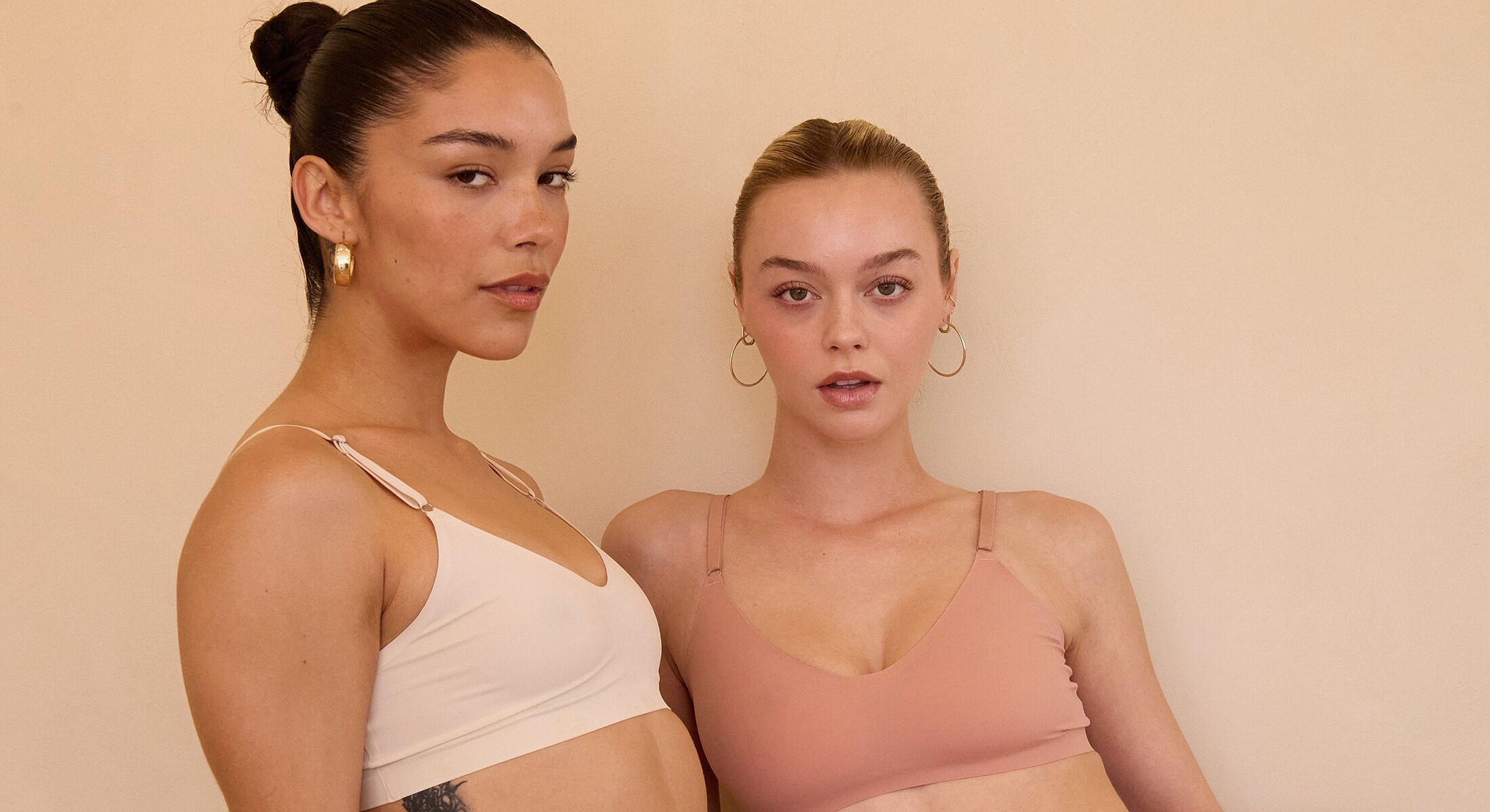 Two women in stylish intimate apparel against beige background.